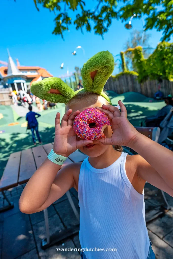 Kind met konijnenoren kijkt door een roze donut in Liseberg, Göteborg.
