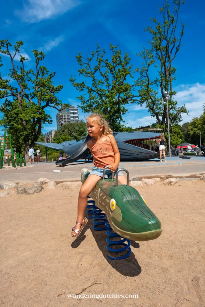 Kind speelt op de grote speeltuin in park Slottsskogen in Göteborg met houten dieren en glijbanen.