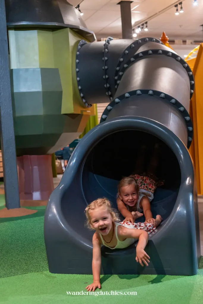Twee kinderen glijden lachend uit een glijbaan in de speeltuin van Universeum Göteborg.