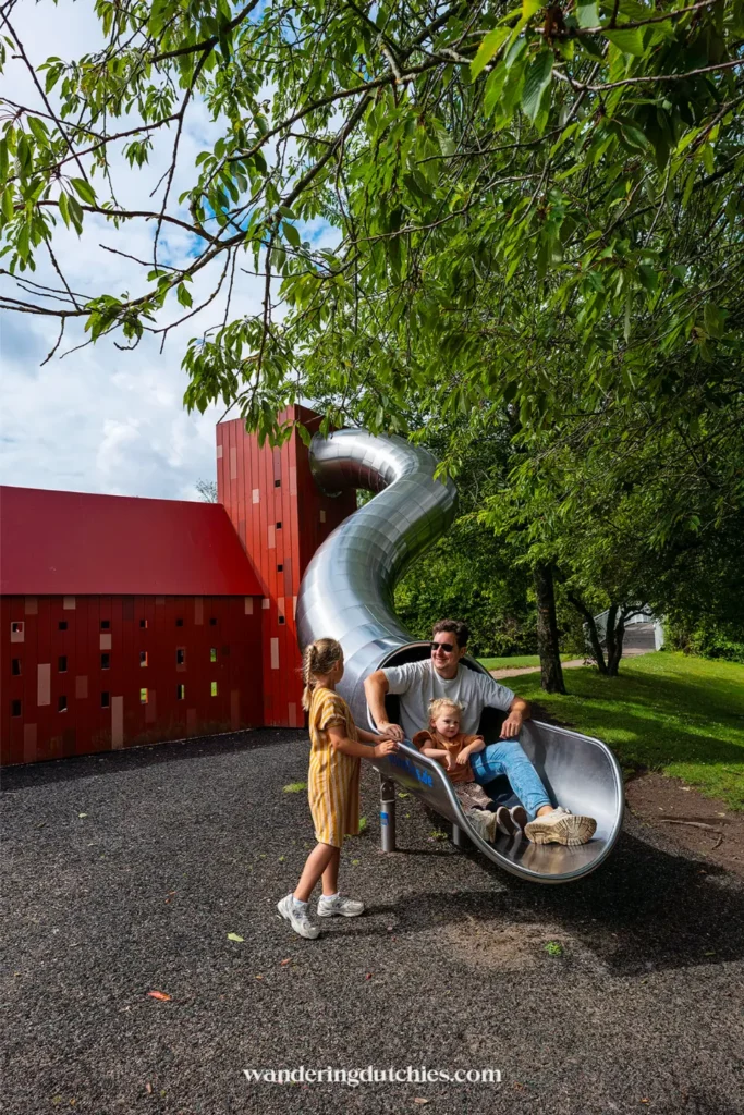 Vader met twee kinderen bij een grote glijbaan naast een rood gebouw in Kolding, Denemarken.