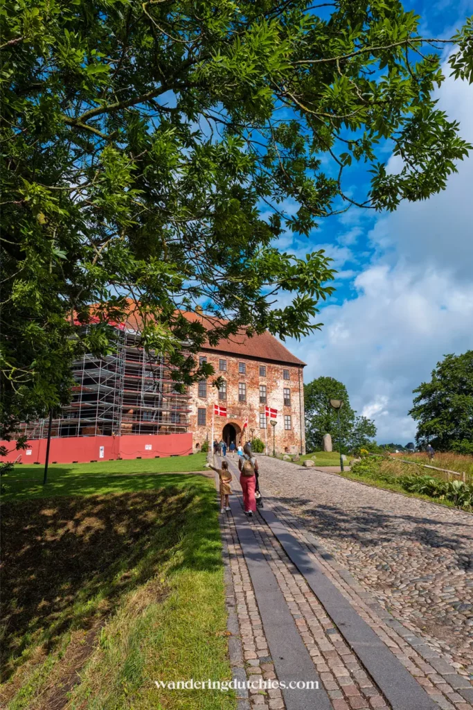 Gezin loopt richting Koldinghus kasteel in Kolding, Denemarken, met Deense vlaggen bij de ingang