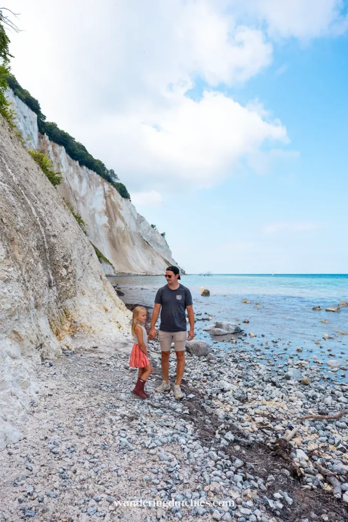 Vader en kind lopen over het stenen strand onder de kliffen van Møns Klint in Denemarken