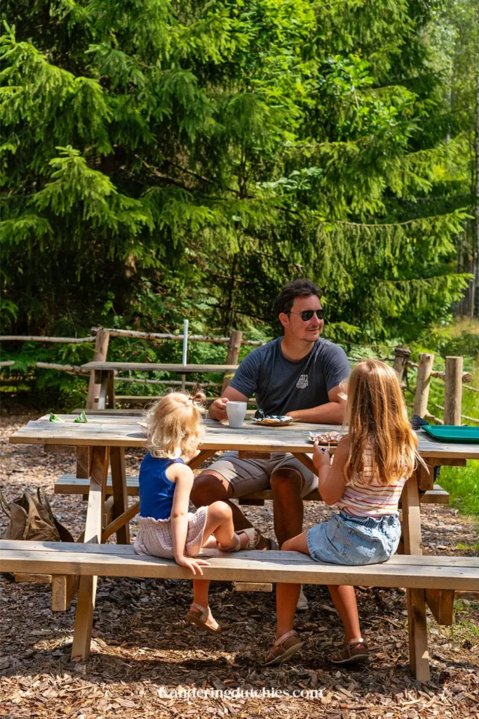 Vader en kinderen hebben een fika aan een picknicktafel in het bos bij Dalslands Moose Ranch in Zweden