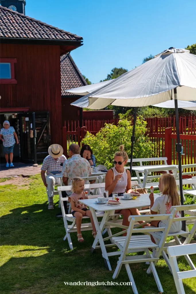 Gezin zit buiten op het terras tijdens fika in Mora, Zweden, met taart en ijsjes op tafel