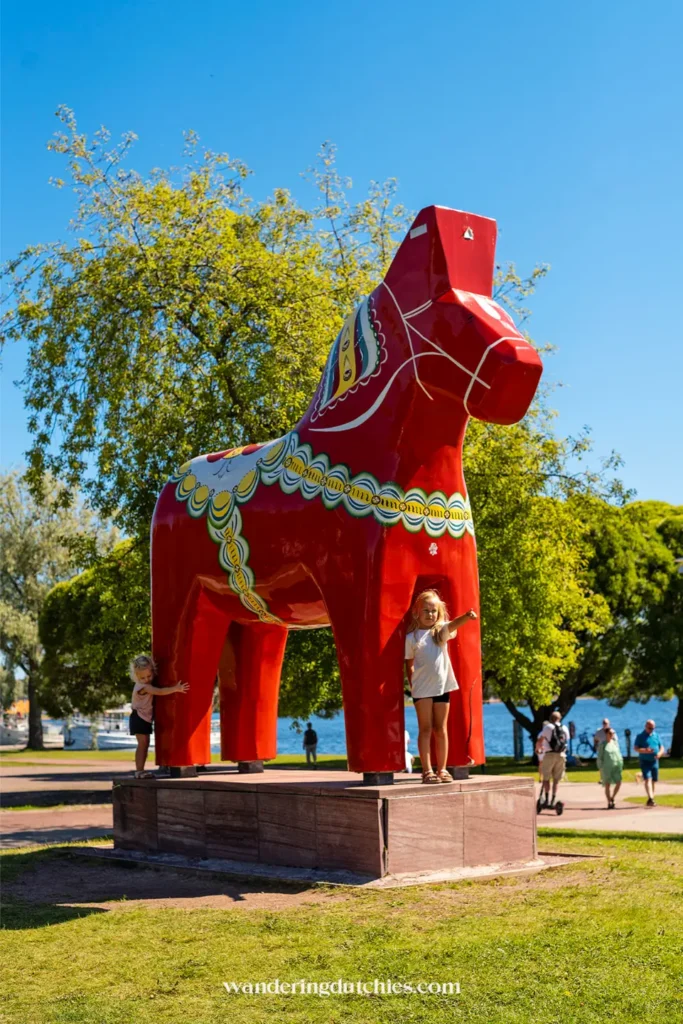 Kinderen poseren bij een groot, rood Dalapaard in Mora, Zweden