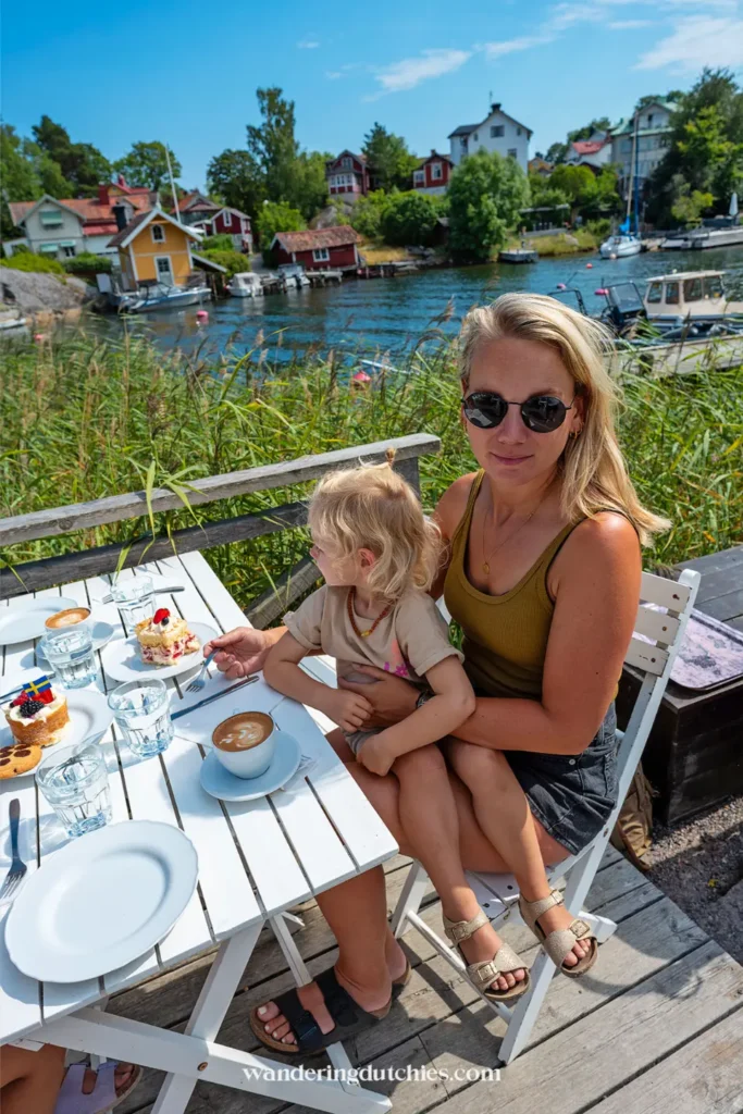 Moeder en kind drinken koffie en eten taart op een terras van Hembygdsgårds Café aan het water in Vaxholm, Zweden
