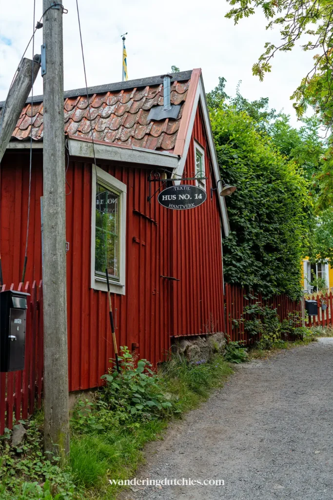 Rood houten huis in Vaxholm met bord Hus No 14 en groen pad langs traditionele Zweedse bebouwing