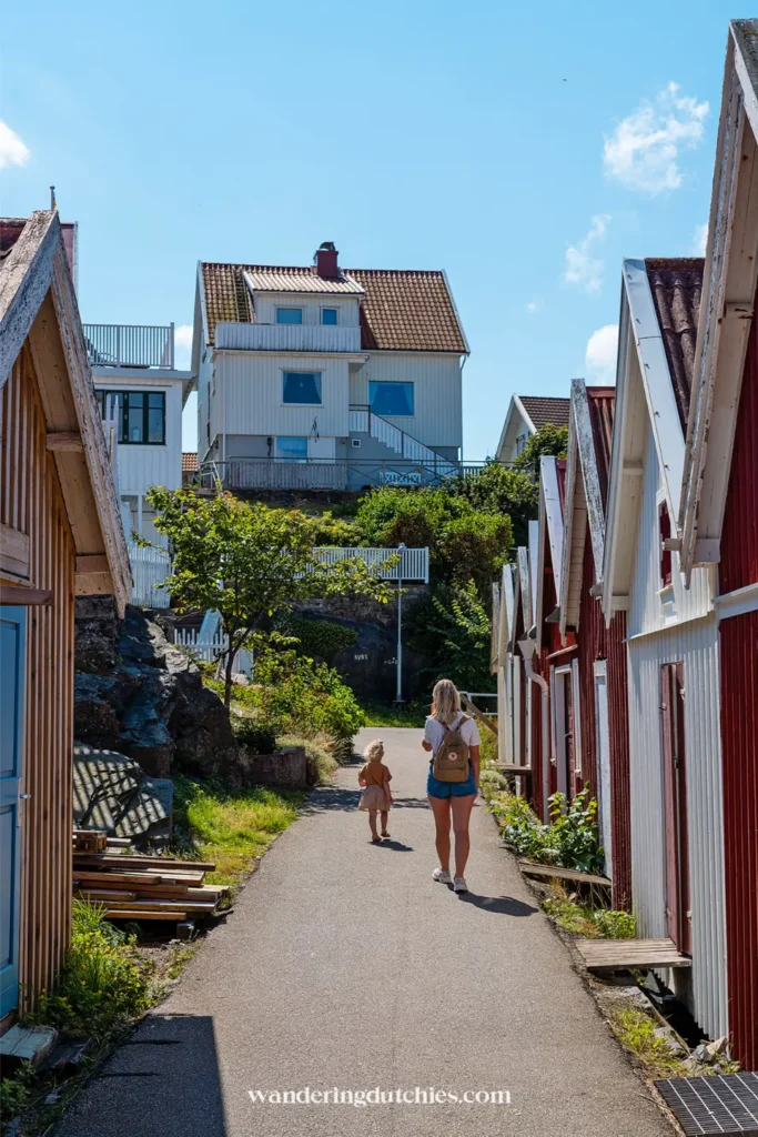 Moeder en kind lopen door een smal straatje tussen houten huisjes op Åstol, Zweden