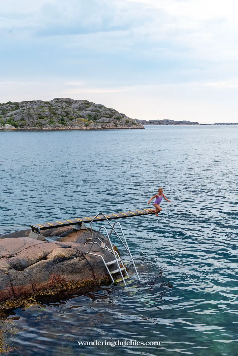 Kind springt van duikplank in zee bij rotsachtige kust van Zweden