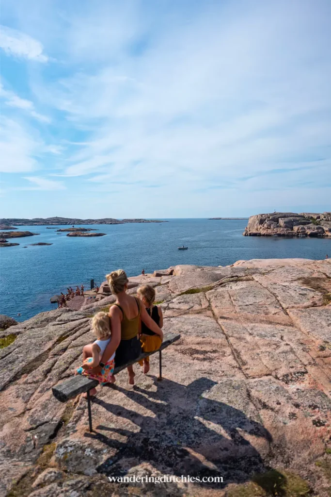 Moeder met twee kinderen op een bankje met uitzicht over zee en rotsen bij Smögen, Zweden