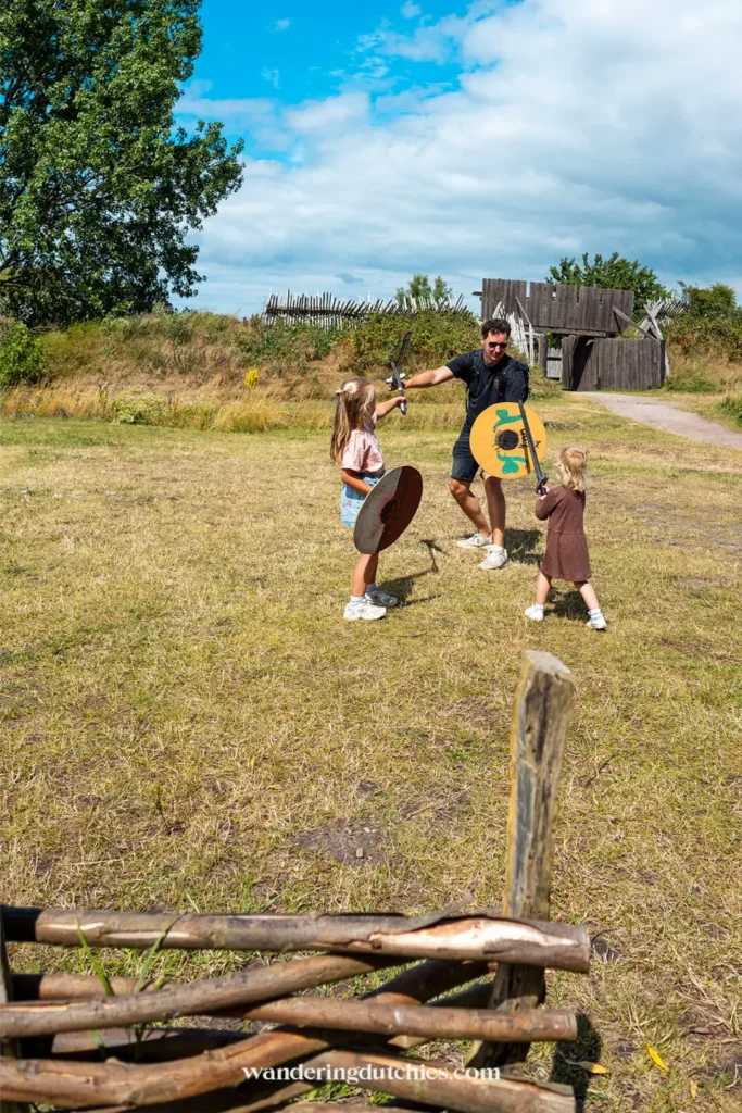 Vader en kinderen spelen vikingen met zwaarden en schilden in het Foteviken Viking Museum in Zuid-Zweden