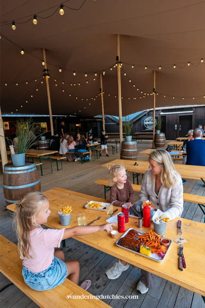 Gezin eet BBQ bij Smokey BBQ in Zuid-Zweden, onder een grote tent met lichtjes