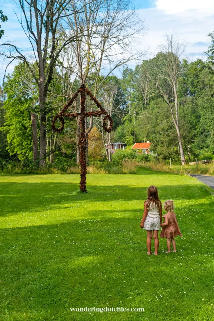 Twee jonge kinderen staan op een grasveld in Röttle en kijken naar een groot houten kunstwerk in de vorm van een huis
