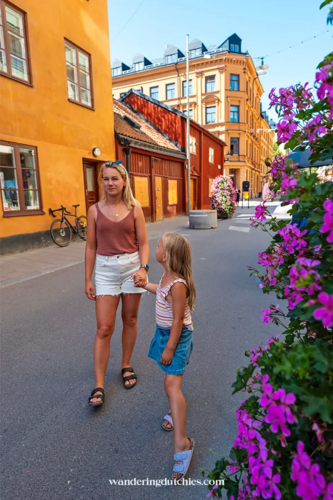 Moeder en dochter lopen hand in hand door een straat met gele en rode houten huizen in Stockholm