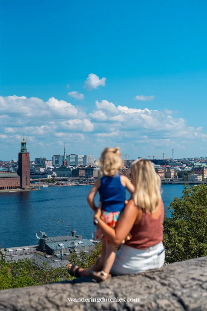 Moeder met kind op schoot kijkt uit over het water en de skyline van Stockholm bij het stadhuis