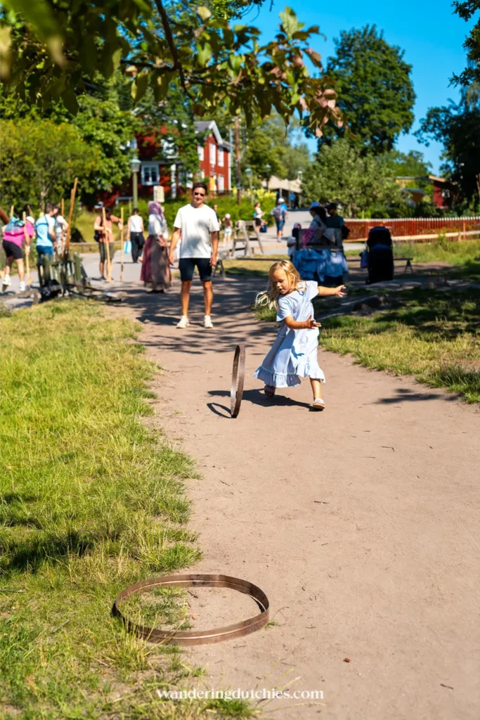 Meisje in blauwe jurk speelt een oud Zweeds ringenspel op een zandpad in Skansen openluchtmuseum in Stockholm