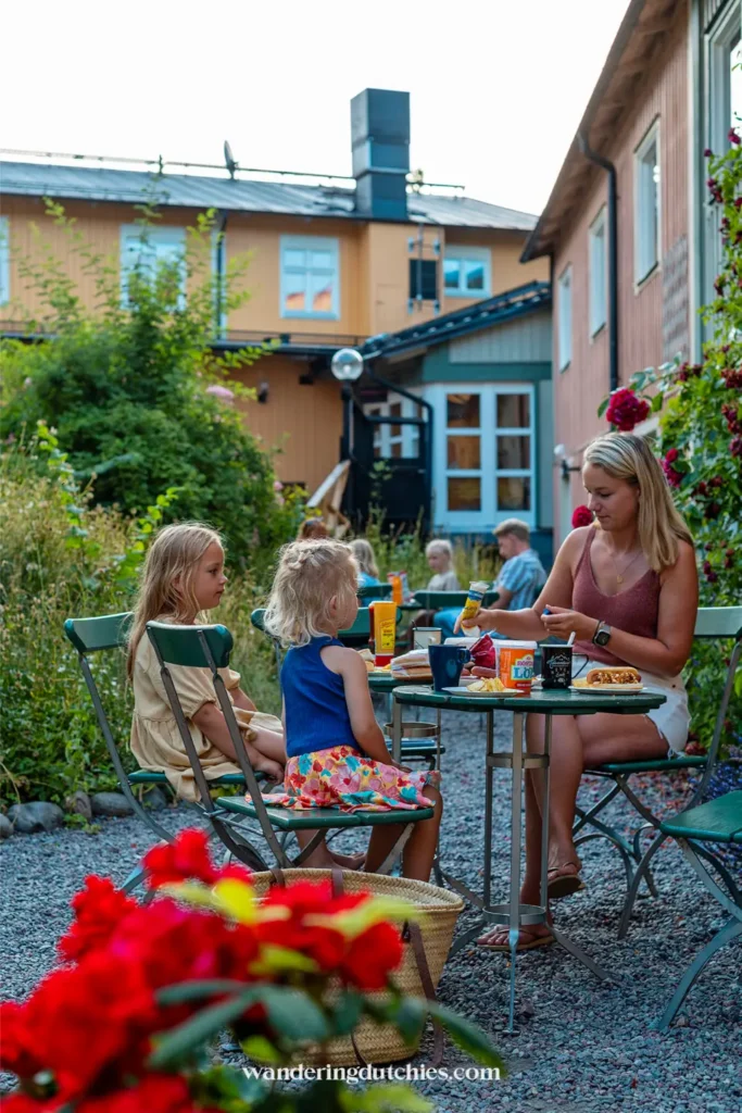 Moeder eet met twee kinderen aan een groene tafel op een sfeervolle binnenplaats bij Zinkensdamm Hostel in Stockholm