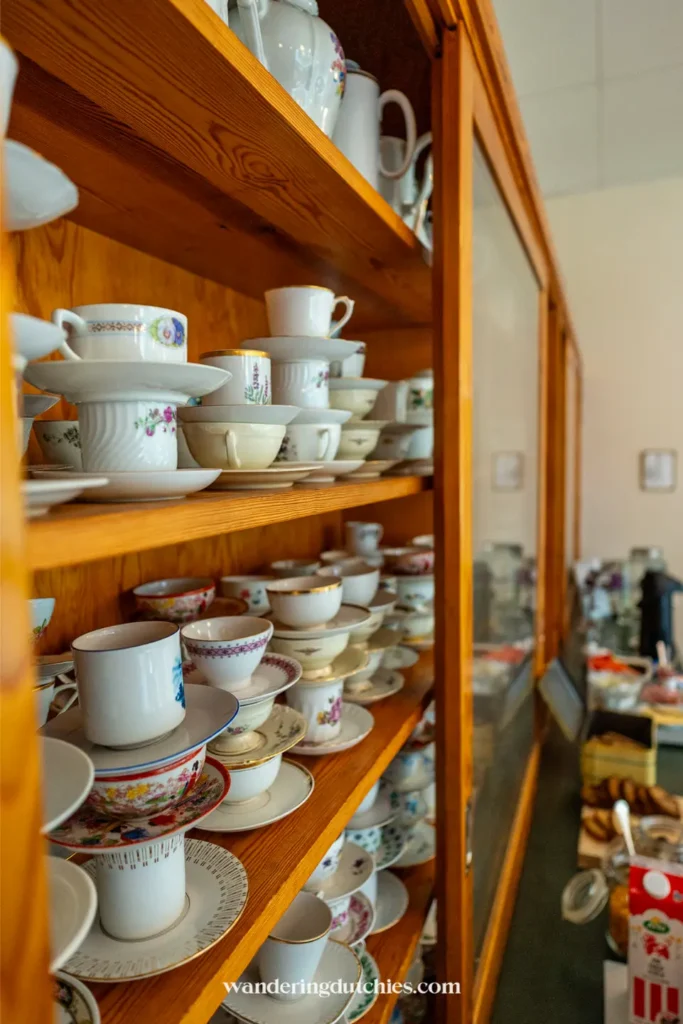 Houten kast vol vintage kopjes en schoteltjes in een café bij Store Mosse