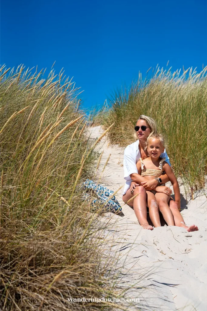 Moeder en jong kind zitten samen in het zand tussen hoge duingrassen bij Sandhammaren strand