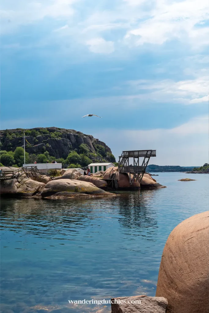 Rotsachtige kust bij Bovallstrand met houten duikplatform, kleine strandhuisjes en rustige zee onder dramatische wolken