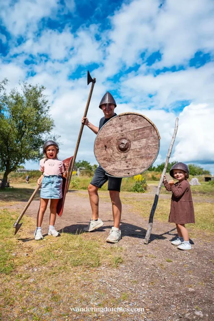 Vader en twee kinderen verkleed als Vikingen met helmen, schild en bijl bij openluchtmuseum Fotoviken in Zuid-Zweden