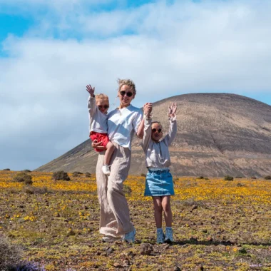 Gezin met kinderen in een vulkanisch landschap op Lanzarote met gele bloemen en een berg op de achtergrond.