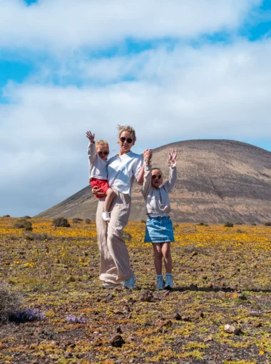 Gezin met kinderen in een vulkanisch landschap op Lanzarote met gele bloemen en een berg op de achtergrond.