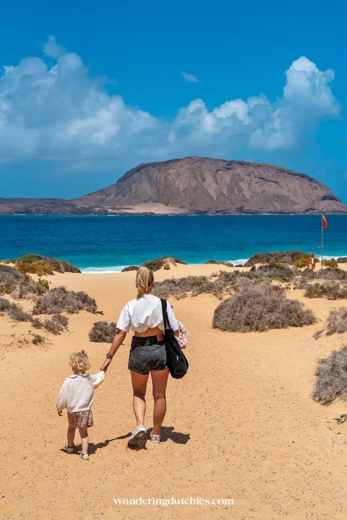 Moeder en kind lopen door de duinen naar het strand op La Graciosa.