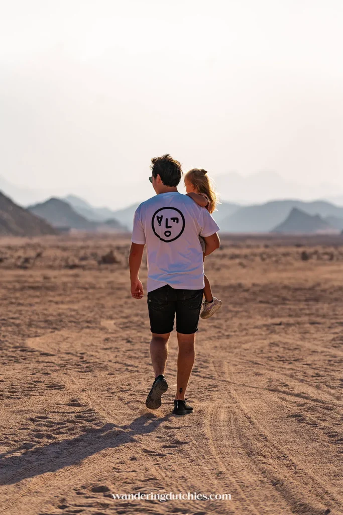 Vader loopt met kind door het woestijnlandschap van Hurghada bij zonsondergang.