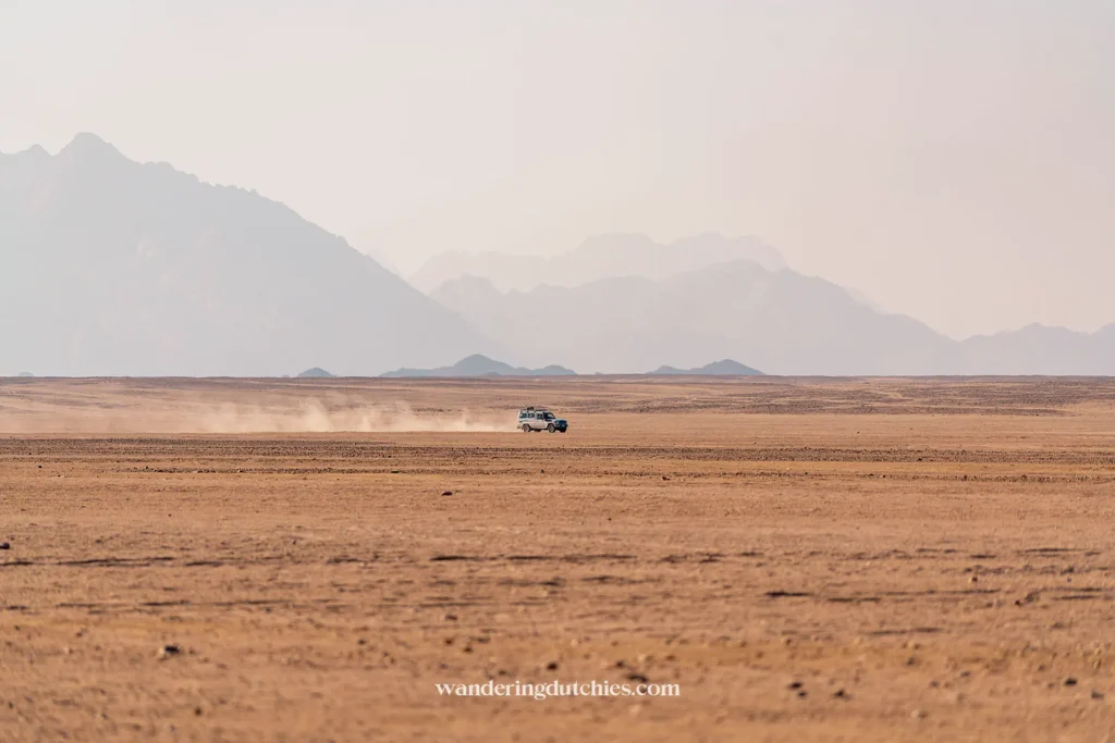 Jeep rijdt door de open woestijn met stofwolken op de achtergrond.