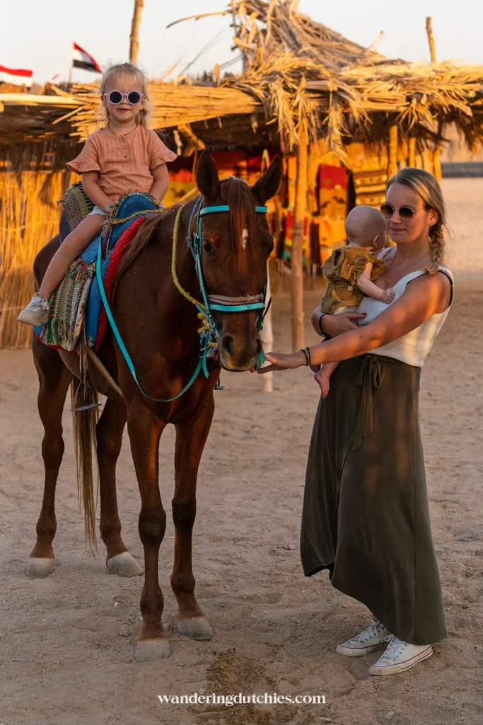 Moeder met baby naast kind op een paard in een woestijndorp.