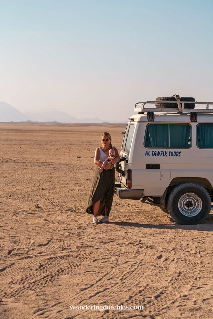 Moeder met baby staat naast een jeep in de woestijn.