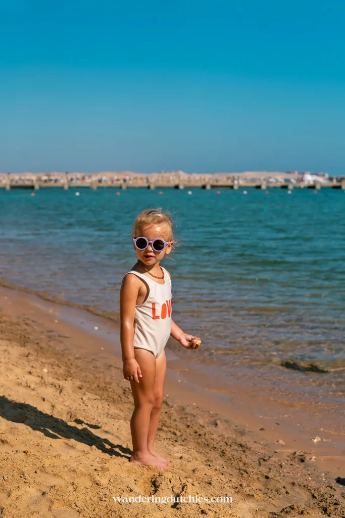 Kind met zonnebril staat op het strand aan de Rode Zee.