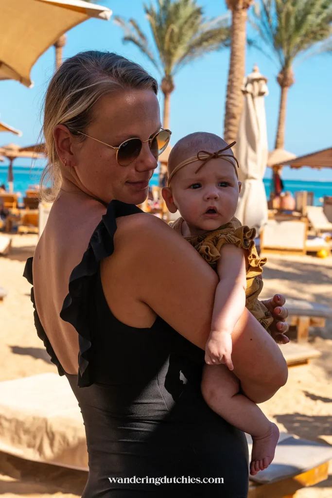 Moeder met baby op de arm bij een strand in Hurghada met palmbomen op de achtergrond.
