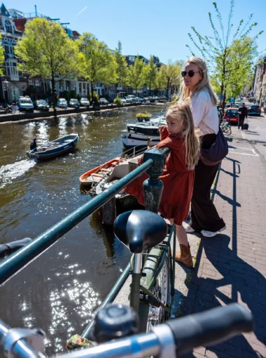 Amsterdam canal with a bicycle in the foreground as a mother and daughter look out over the water on a sunny spring day.