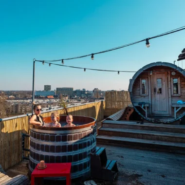 Familie ontspant in een houten hottub op het dakterras van Volkshotel in Amsterdam.