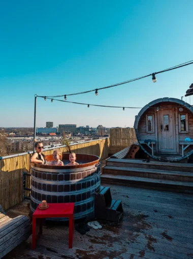 Family relaxing in a wooden hot tub on the rooftop terrace of Volkshotel in Amsterdam.
